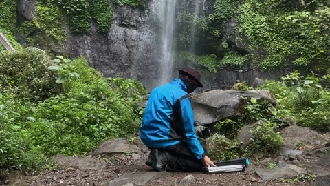 Hiker Assembling Chair, Waterfall Background, Lush Jungle, Static Shot Stock Footage 324850412