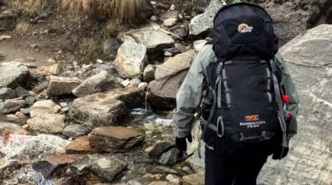 Hiker with backpack cross the mountain stones river. Himalayas Nepal HD video Stock Footage 64829302
