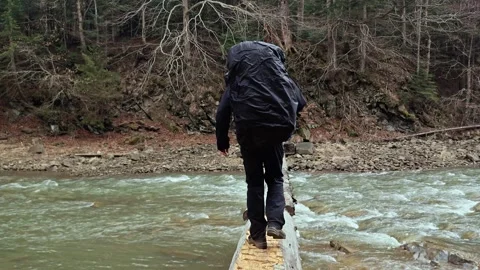 Hiker with Backpack Crossing Mountain River on Log Bridge Back View 4K Video stock 335098892