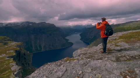 Hiker with backpack enjoying the view, standing on top of the mountain in Norway Stock Footage 99707387