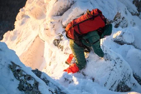 Hiker with backpack going thru rocks, wind and snow on the mountain peak at cold Stock Photos