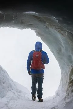 Hiker with Backpack Inside Ice Cave Facing Bright Exit Stock Photos