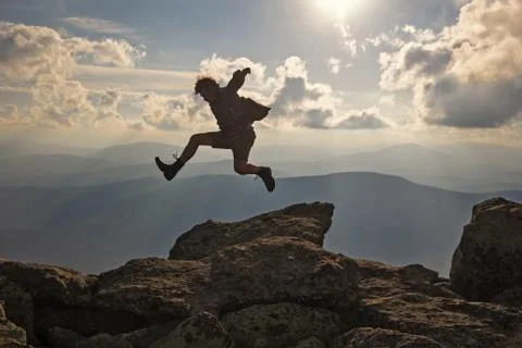 Hiker with backpack jumping over rocks  sunset sky on the background Stock Photos