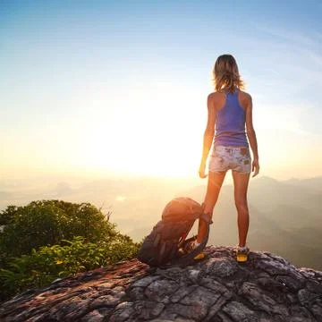 Hiker with backpack standing on top of a mountain and enjoying sunrise Stock Photos
