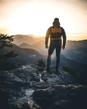 Hiker with backpack standing on top of a mountain and enjoying sunrise. Stock Photos