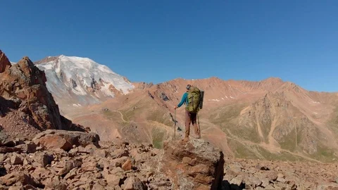 Hiker with a backpack stands on a large stone in the mountains Stock Footage 122266228