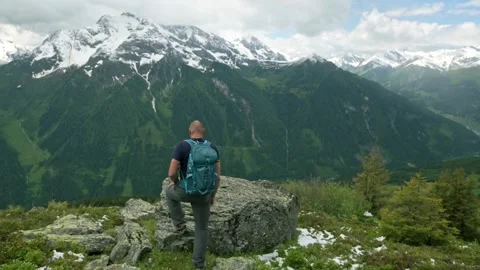Hiker with backpack stands on mountain trail, surrounded by rocky terrain and Stock Footage 282231013