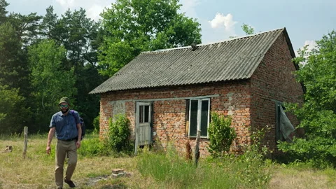 Hiker with backpack walking away from old abandoned brick house Stock Footage 339588335