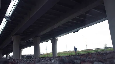 Hiker with backpack walking under bridge. Car traffic on city road at background Stock Footage 80286377