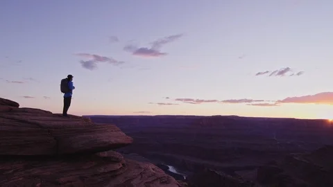 Hiker with Backpack walks to cliff edge and overlooks canyon Stock Footage 127060686