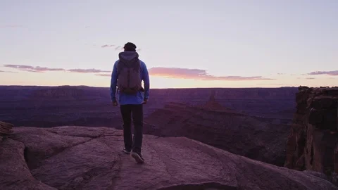 Hiker with Backpack walks to cliff edge and overlooks canyon Stock Footage 127061167