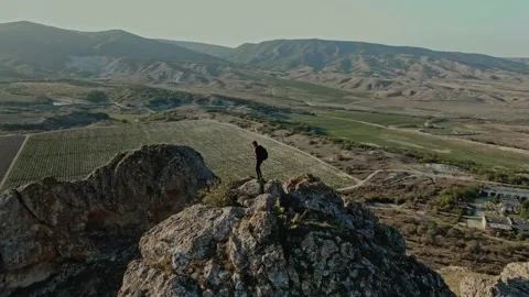 A Hiker in a Baseball Cap with a Backpack Climbs a Rocky Top of a Mountain on th Stock Footage 150592551