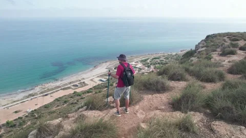 A hiker in a cap, with a backpack and sticks walks on the edge of the escar.. Video stock 224473320