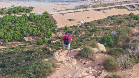 A hiker in a cap, with a backpack and sticks stands on the edge of a cliff .. Stock Footage 228616315