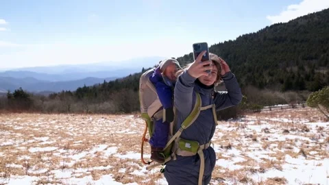 A hiker captures a selfie while carrying a baby in a backpack, exploring the Stockbeeldmateriaal 280370193