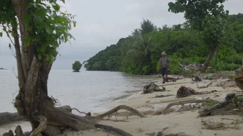 Hiker carrying a red backpack walking alone along a tropical beach Stock Footage 344699816