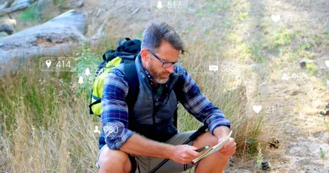 Hiker crouching on trail, tapping tablet with stylus checking route and causing Video stock 333719860
