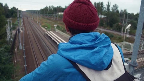 Hiker dressed in jacket and knitted hat with backpack standing on railway bridge Stock Footage 80054658