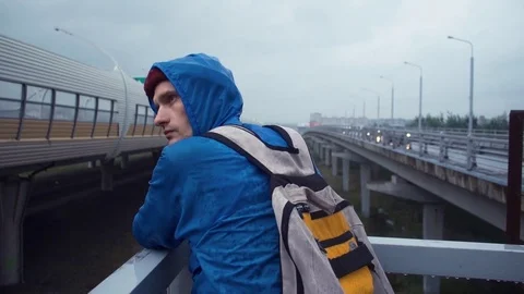 Hiker dressed in jacket and knitted hat with backpack standing on road bridge Stock Footage 80286473