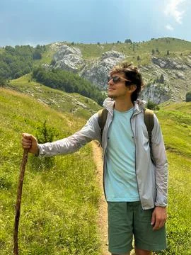 Hiker enjoying the view while walking through green hills with rocky peaks Stock Photos