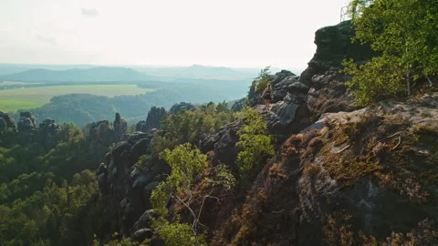 A hiker explore rocky cliffs overlooking a vast landscape of rolling hills and Stock Footage 284332475