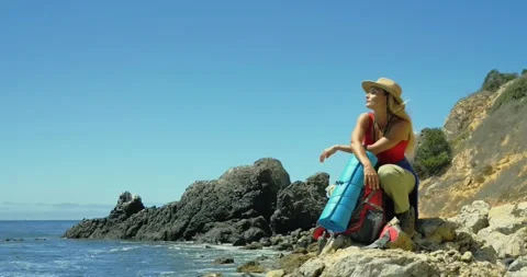 Hiker Exploring Rocky Beach with Backpack under a Clear Sky Видео 323543639