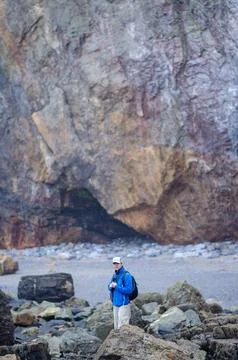 Hiker Exploring Rocky Beach with Dramatic Cliff Background, Adventure Travel Stock Photos
