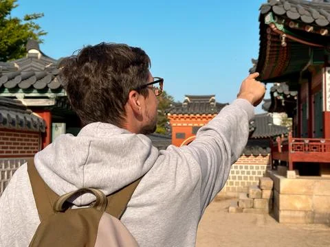 Hiker with glasses and backpack points to the ancient Korean Palace Stock Photos