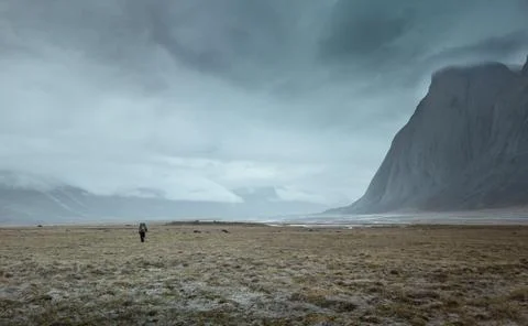 Hiker with a heavy backpack walking under majestic rocks in remote arctic valley Stock Photos