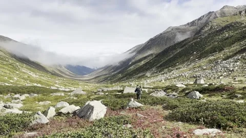 A hiker with a large backpack walking along a mountain valley, peaks of rocky Stock Footage 252882170