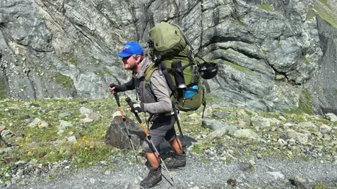 A hiker with a large backpack walks along a mountain trail Video stock 158226544