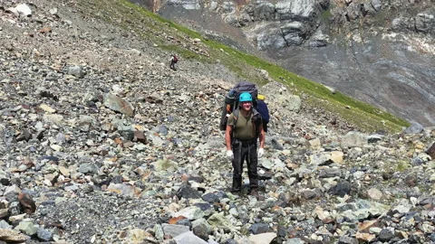 Hiker with a large backpack walks uphill along the scattering of stones Video stock 158018787