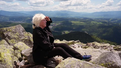 A hiker looks into the distance while sitting on rocks. Stock Footage 311256190