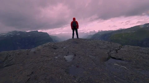 Hiker man with a backpack standing on the edge of the mountain in Norway in Stock Footage 99708075
