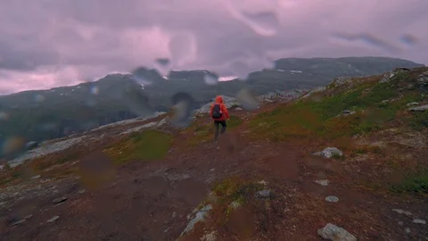 Hiker man with a backpack walking on mountain terrain in Norway in rainy weather Stock Footage 99708025