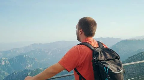 Hiker man from behind with a backpack sitting on top of the mountain. Stock Photos