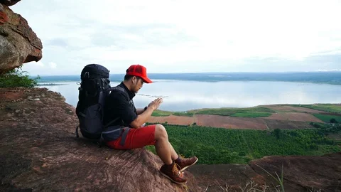 Hiker man sitting and using smartphone on the edge of cliff Stock Footage 128215685