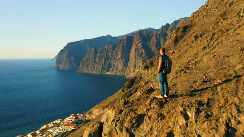 Hiker man standing on mountain top and enjoying ocean view at sunset. Boy Stock Footage 227212448