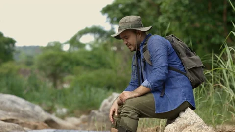Hiker man taking rest at river in mountains. Hiker man with a backpack touching  Video stock 158789546