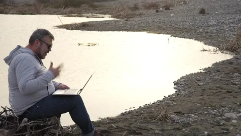 Hiker man using laptop by coast lake. Adult man is holding laptop Stock Footage 238526454