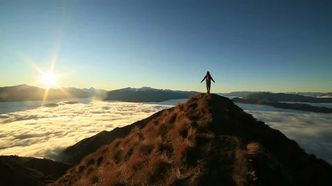Hiker on mountain top above clouds, arms outstretched  Stock Footage 75970074