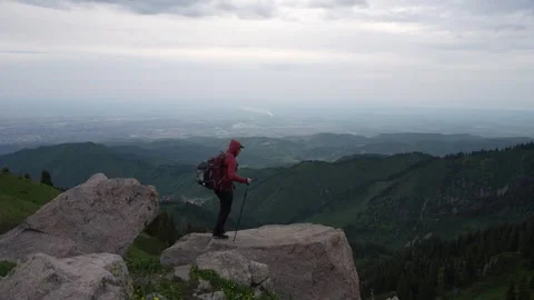 Hiker in red jacket stands on rock, gazing at expansive mountain view Vídeos de archivo 340392267