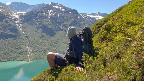 Hiker relaxes on a mountain top and enjoys view over  beautiful turquoise lake Stock Footage 156786053
