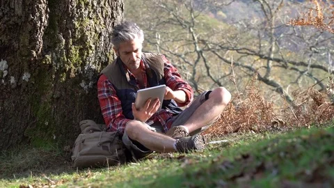 Hiker relaxing by tree looking at map and using tablet Stock Footage 72092348