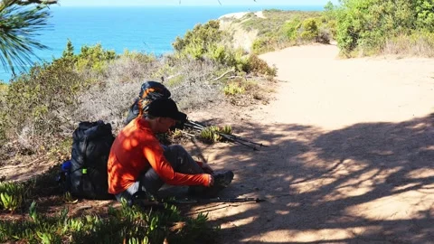 Hiker resting on coastal path preparing to continue trail Portugal Stock Footage 319672510