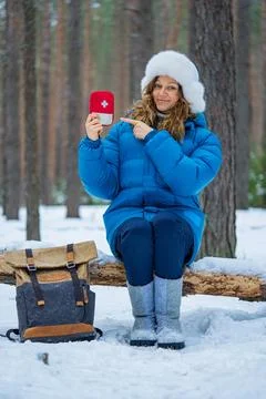 Hiker resting on fallen tree trunk in snow-covered forest, signaling first aid Stock Photos
