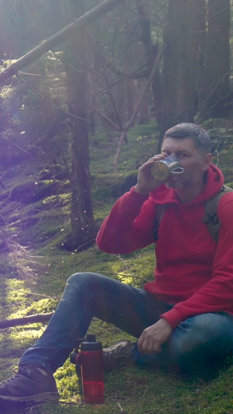 Hiker resting in forest clearing and drinking beverage during trek Stock Footage 337028388