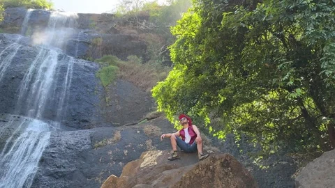 Hiker Resting on Rock, Camera Pans to Tiered Waterfall, Lush Landscape, Wide Pan Stock Footage 324769950