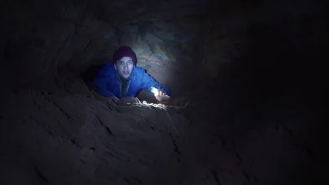 Hiker scrambles in cave hole illuminates way with flashlight in his smartphone Video stock 80053558