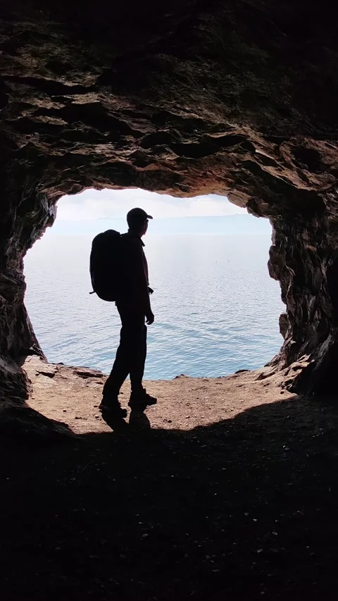 Hiker silhouette exploring sea cave opening. vertical. Stock Footage 335390464